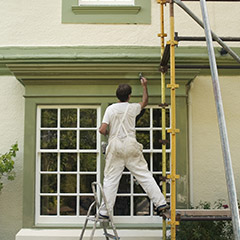 Man on scaffold painting house