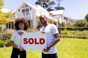 a couple holding a "sold" sign in front of a house they just bought